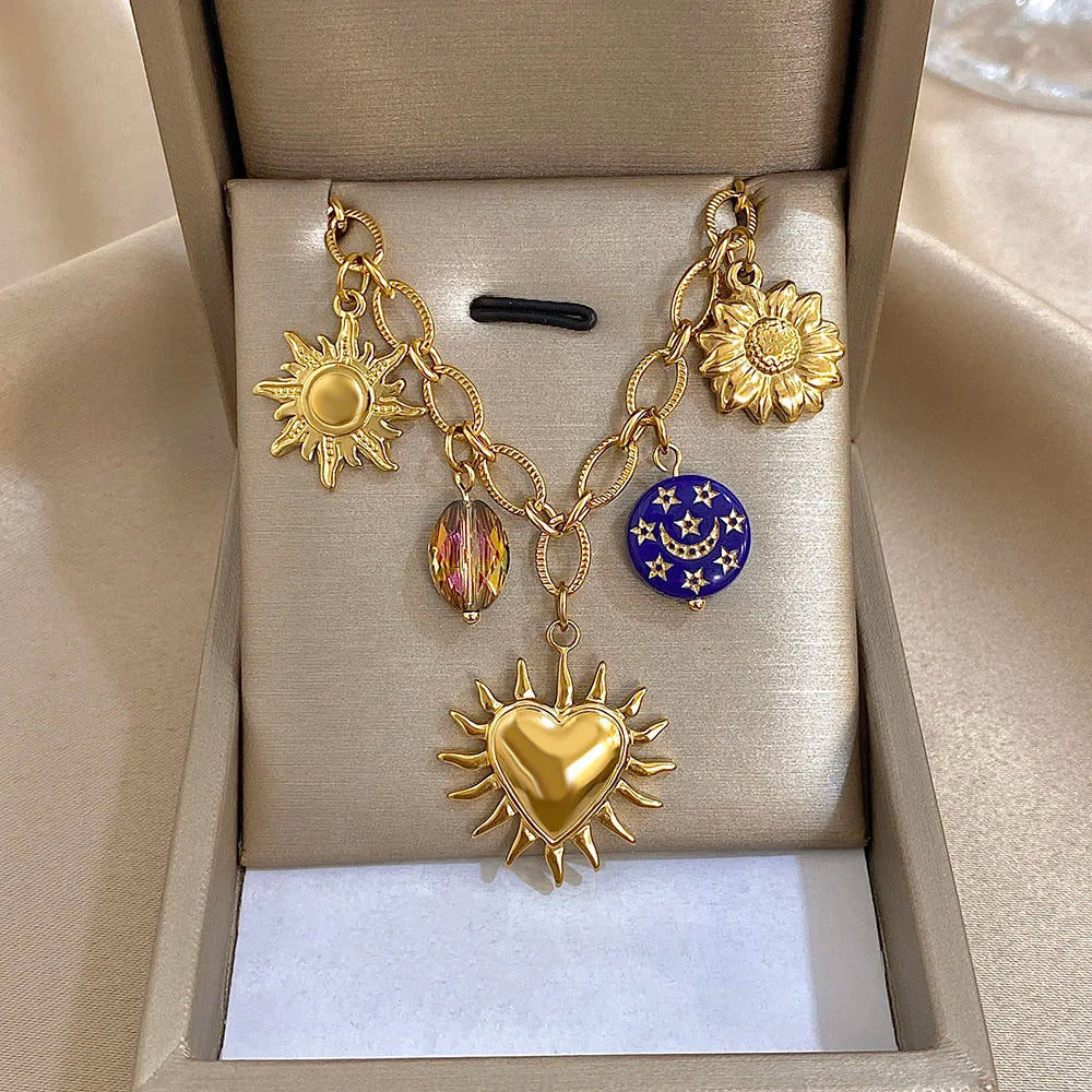 Gold necklace with sun, heart, and flower charms in a beige jewelry box.