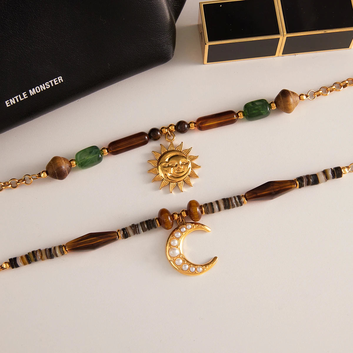 Necklace with sun and moon pendants on a white surface, with 'ENTLE MONSTER' branding in the background.