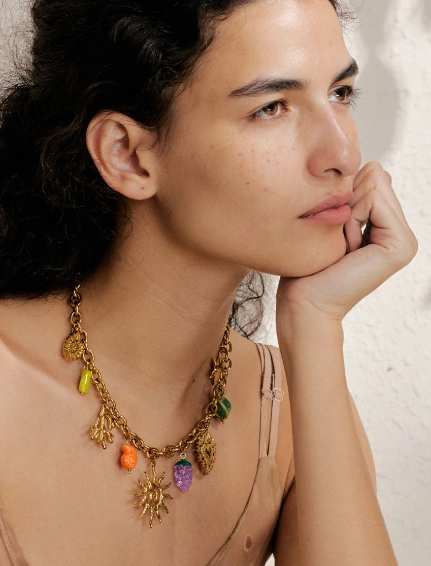 Woman wearing a gold necklace with colorful charms against a neutral background
