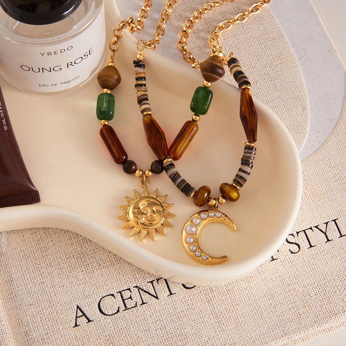 Two beaded necklaces with sun and moon pendants on a white dish, with a Yves Rocher product in the background.