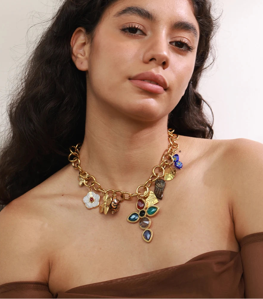 Woman wearing a gold necklace with colorful charms against a neutral background