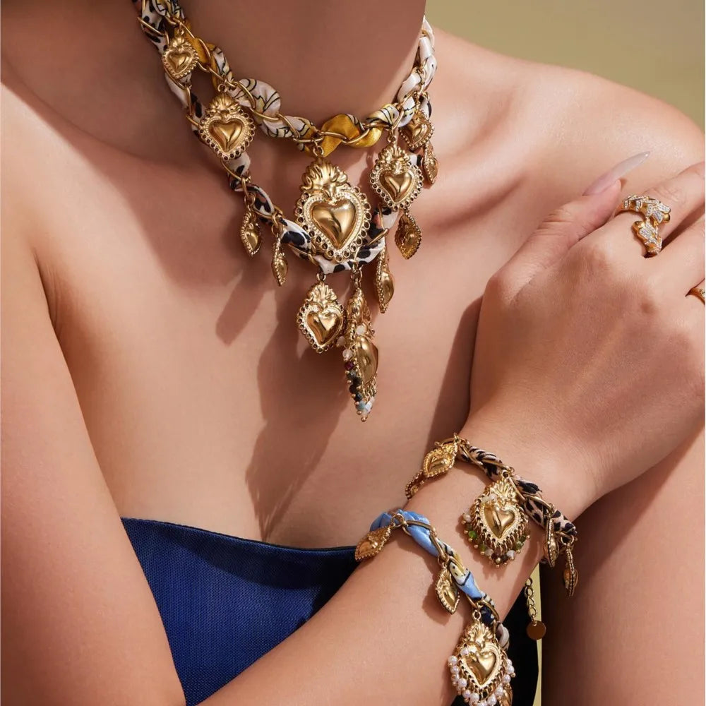 Gold jewelry set including necklace, bracelet, and ring on a person wearing a blue top.