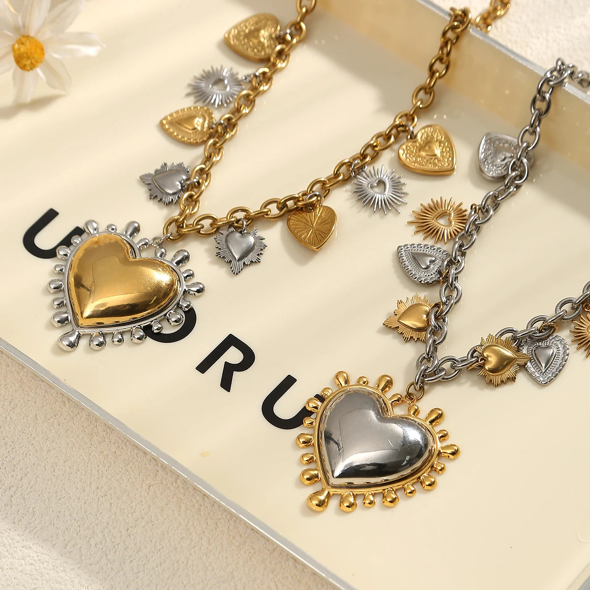 Gold and silver heart-shaped charm necklaces on a branded box.