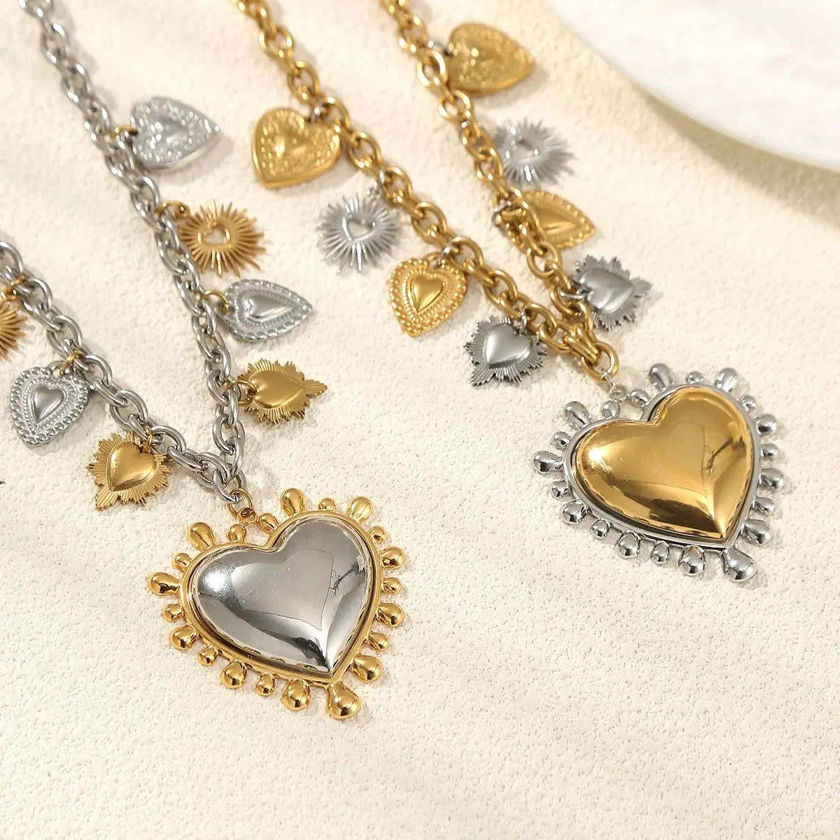 Gold and silver heart-shaped pendants on chains against a beige background