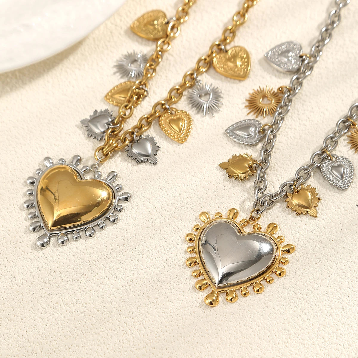 Two heart-shaped pendants on gold and silver chains against a beige background