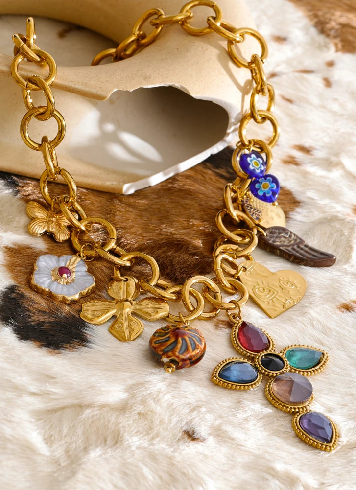 Gold chain bracelet with colorful charms on a textured surface