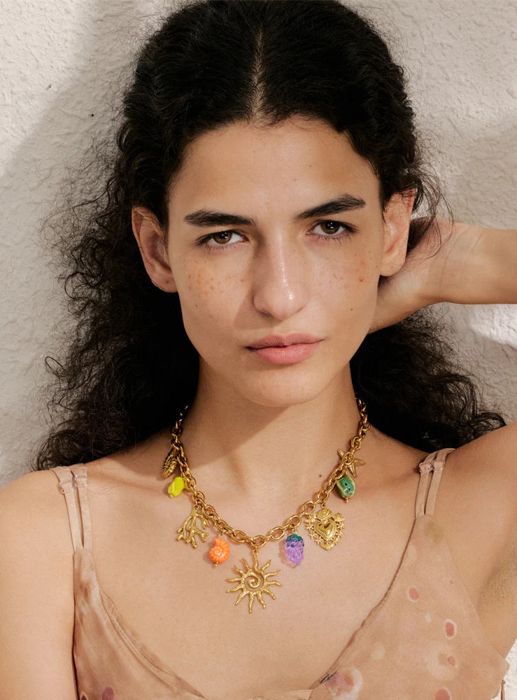 Woman wearing a colorful necklace with various charms against a neutral background